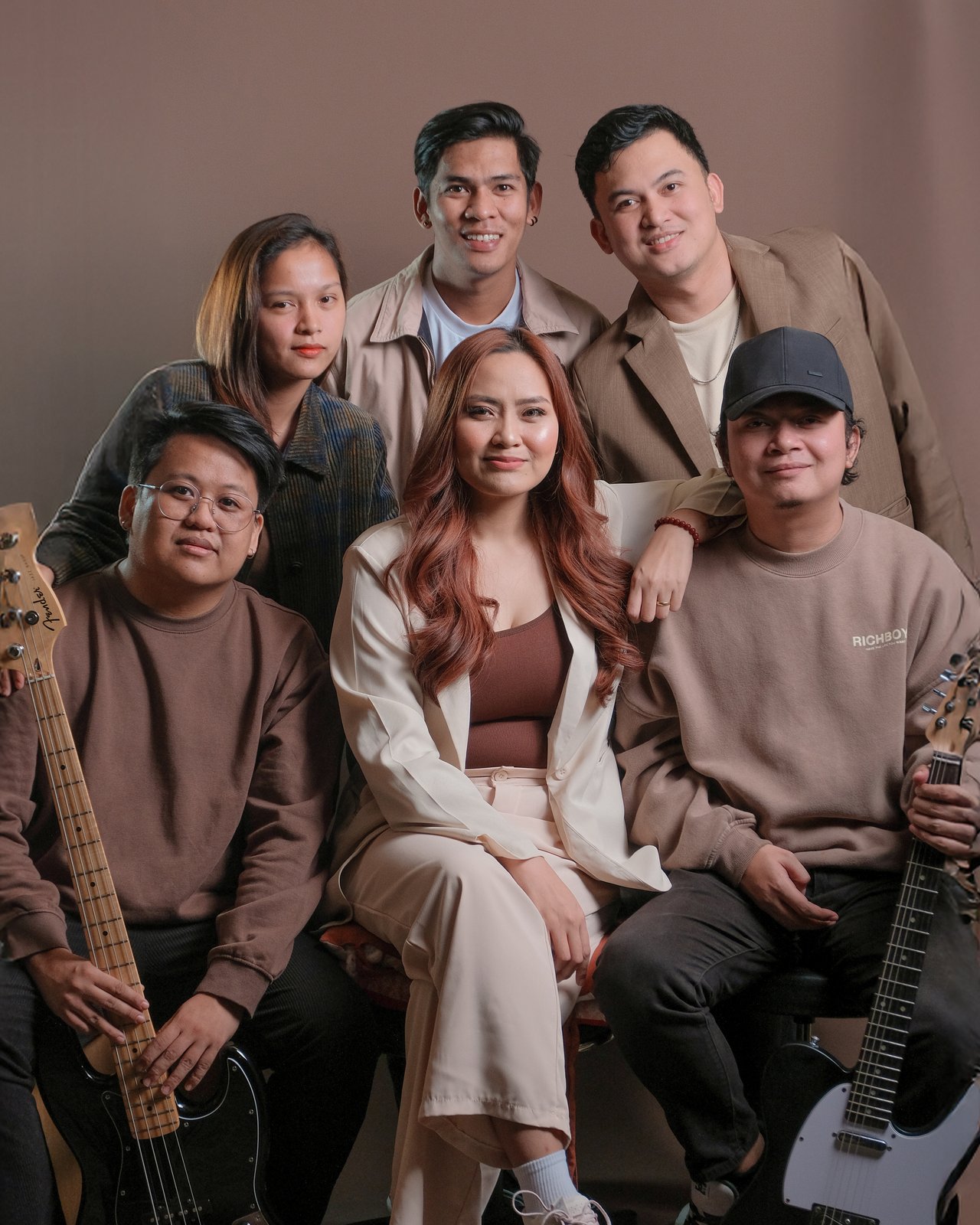 The six members of phoebe in a warm brown portrait shoot, holding bass and guitar
